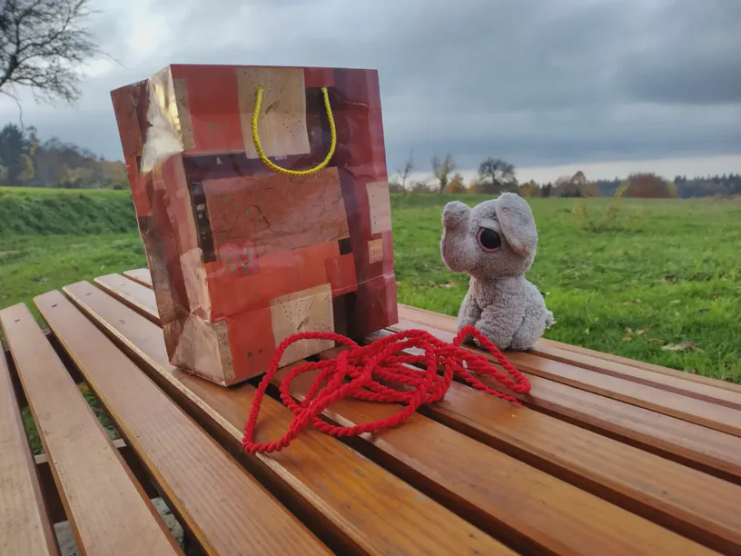 Kleiner Elefant sitzt vor einem roten Seil. Daneben steht eine große Geschenketüte.